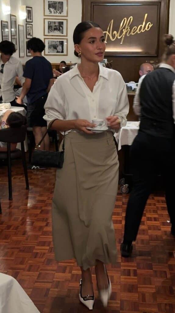 Woman in chic outfit holding teacup at restaurant Alfredo, mingling in a lively, stylish atmosphere.