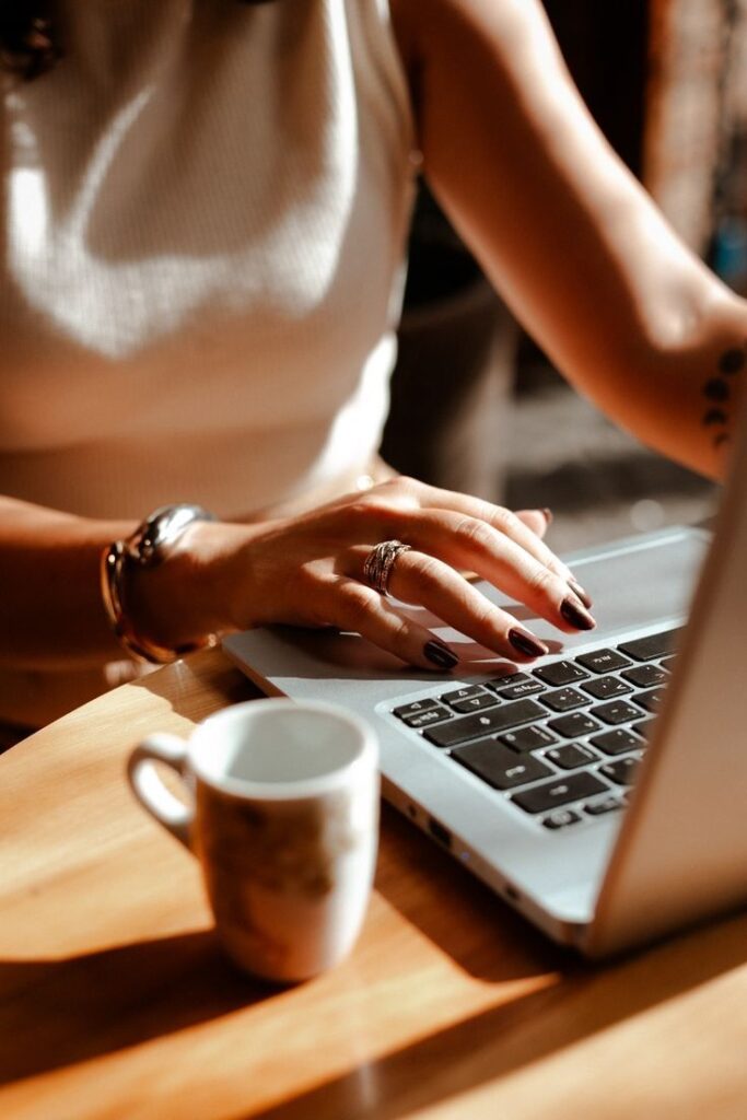Woman typing on laptop with coffee cup nearby, showcasing cozy workspace and focus.