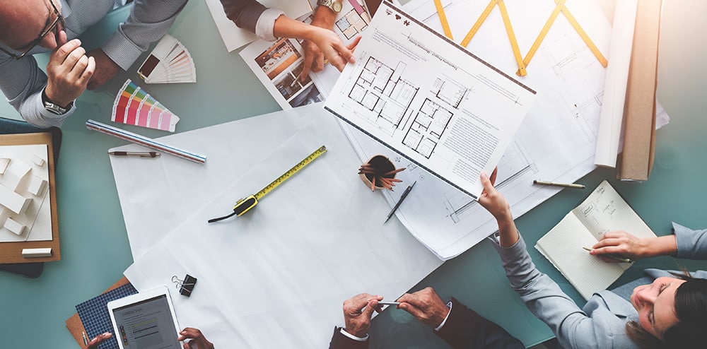 bringing-interior-design-and-construction-together Team reviewing architectural blueprints and planning construction project with tools on a table. | Sky Rye Design Team reviewing architectural blueprints and planning construction project with tools on a table.