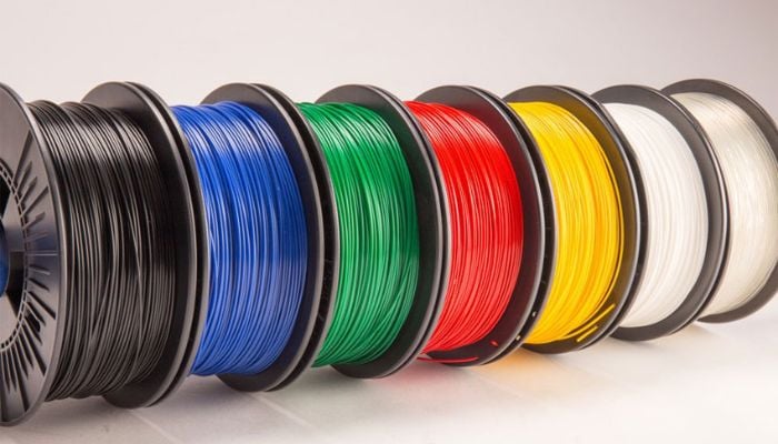 Spools of colorful 3D printer filament in black, blue, green, red, yellow, and white, arranged in a row.