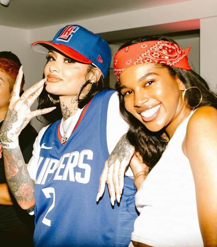 Two friends smiling at a party, wearing a blue Clippers jersey and a red bandana.
