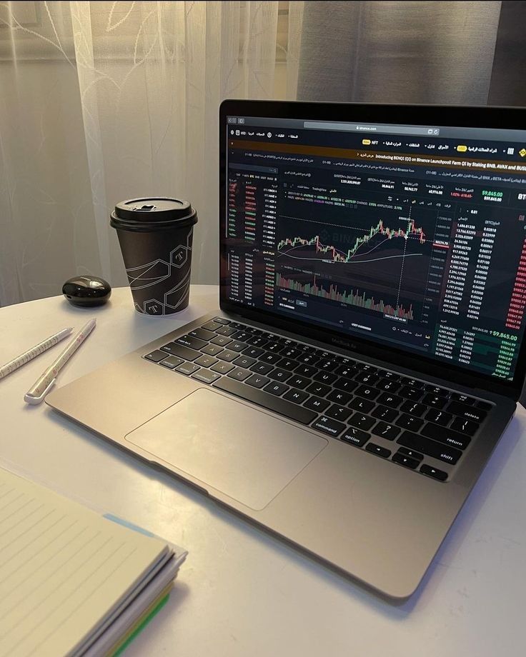 Laptop displaying stock market charts next to a coffee cup on a desk.