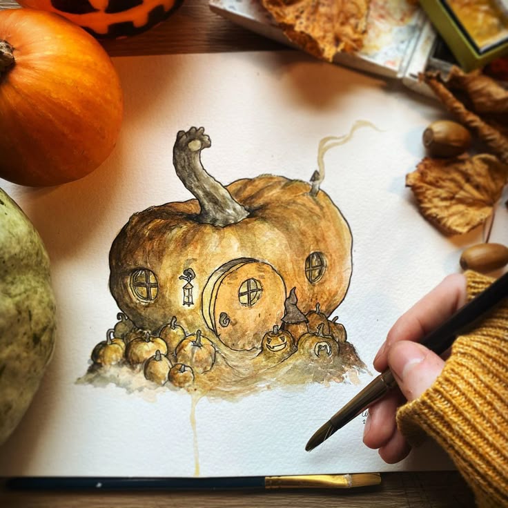 Whimsical pumpkin house watercolor illustration with fall leaves, surrounded by small pumpkins and artist's hand.