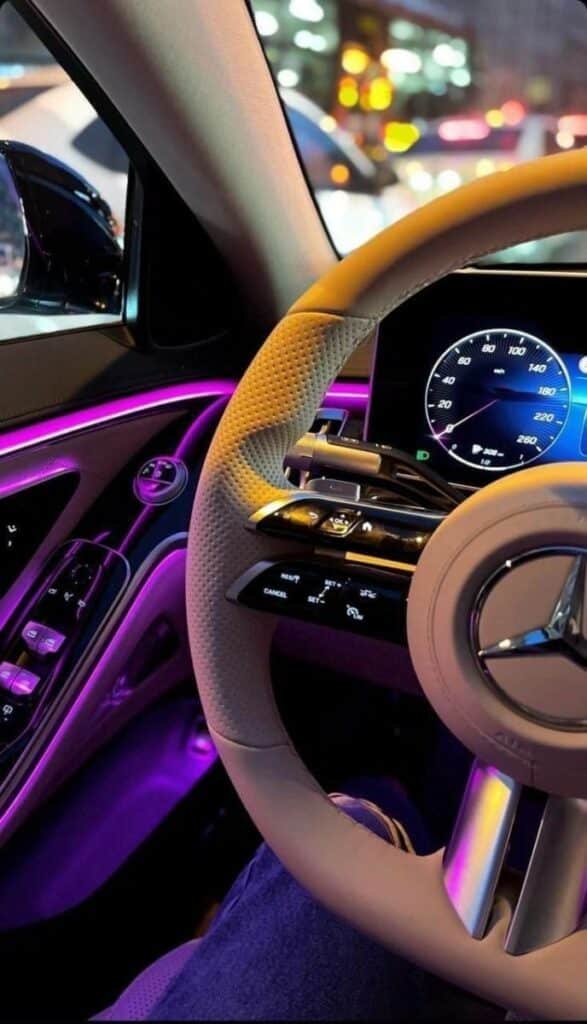 Luxurious car interior with ambient lighting, featuring a modern steering wheel and digital dashboard in vivid colors.