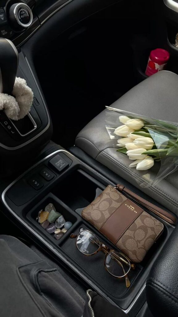 Car interior with a bouquet of white tulips, a Coach wallet, sunglasses, and assorted crystals.