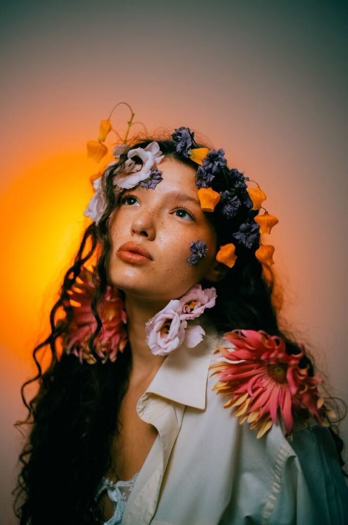 Woman wearing colorful flowers in hair against a warm glowing background. Artistic floral portrait.