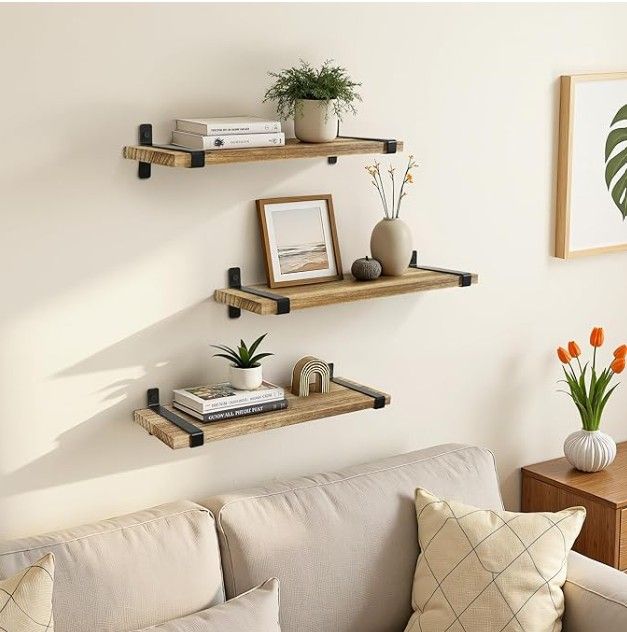 Wooden wall shelves with decor above a beige sofa, showcasing a minimalist design with plants and books.