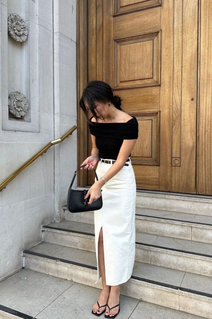 Woman in black top and white skirt with purse on steps, wooden door background.