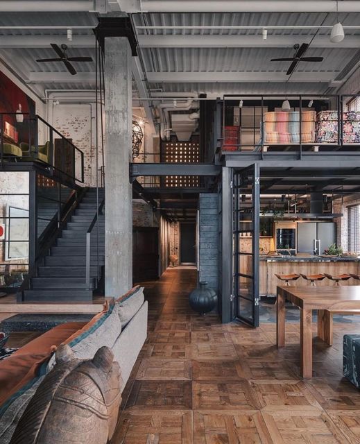 Industrial loft with open layout, modern decor, and mezzanine; wooden floors and exposed beams create a cozy atmosphere.
