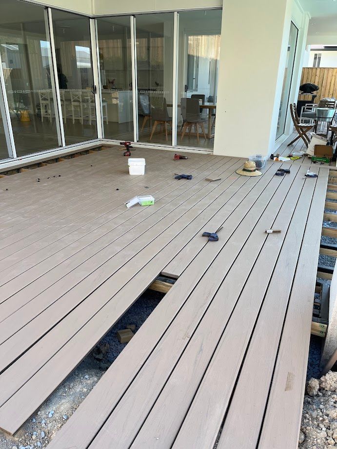 Partially installed outdoor deck with tools and materials on site near a modern patio, ready for completion.