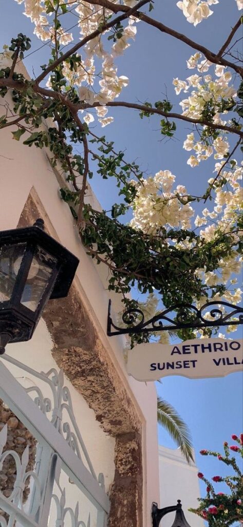 White bougainvillea and Aethrio Sunset Villa sign with lantern against a clear blue sky.