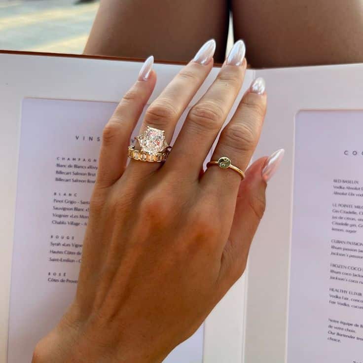 Hand displaying elegant rings over a menu, showcasing stylish jewelry and manicured nails.