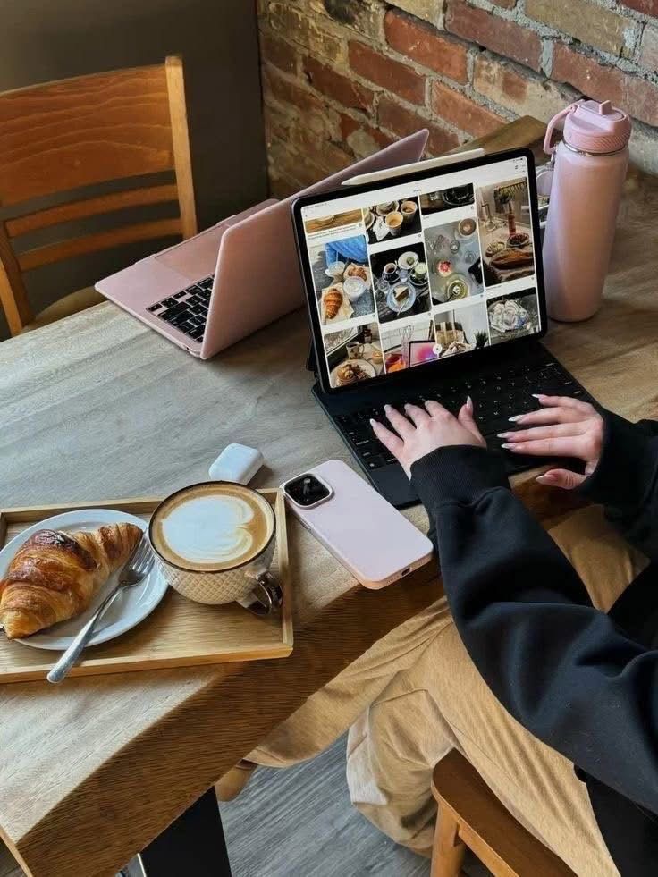Person working on a laptop at a cafe with a croissant and coffee, browsing food photos.