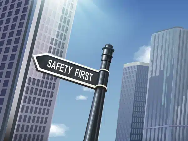 Safety First signpost in a skyscraper-dominated cityscape under a clear blue sky.