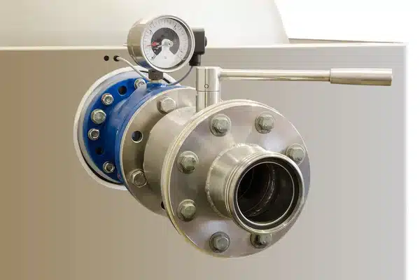 Industrial valve with pressure gauge on stainless steel pipe in a mechanical setting.
