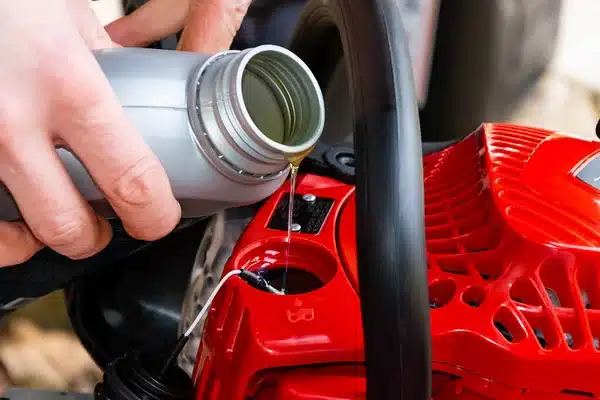 Pouring oil into a small engine: person adds oil to red garden machine for maintenance.