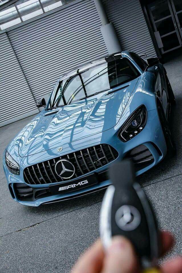 Sleek blue Mercedes-AMG sports car in a showroom, with a hand holding the car key fob in focus.