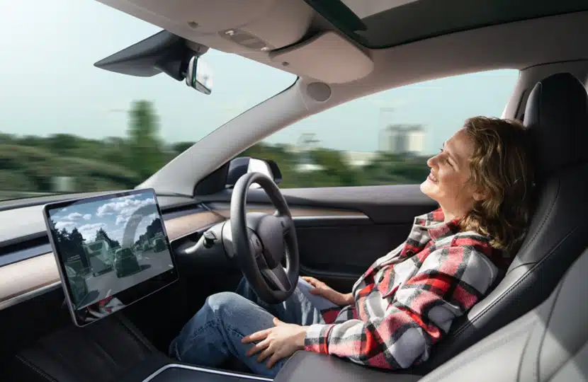 Woman relaxing in self-driving car with hands off the wheel, enjoying autonomous driving technology on open road.