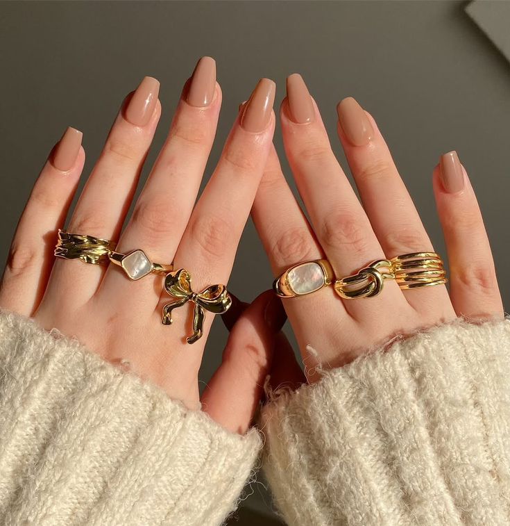 Hands showcasing stylish gold rings with nude manicured nails, wearing cozy cream sweaters.