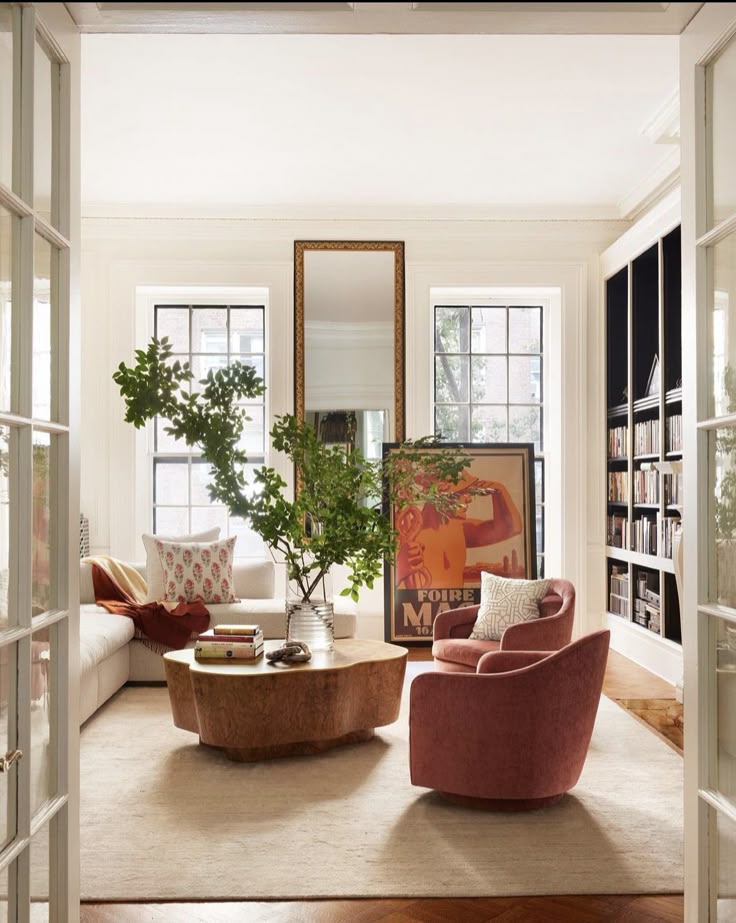 Stylish living room with modern furniture, large mirror, and bookshelf, featuring a wooden coffee table and potted plant.