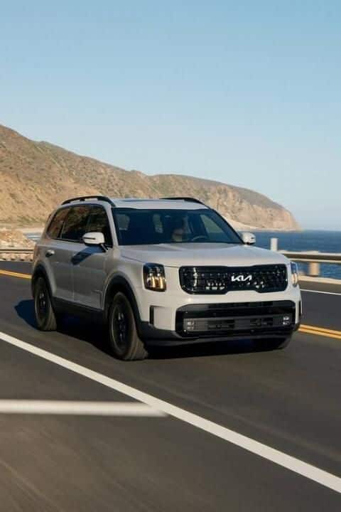 SUV driving on a coastal highway with scenic ocean and mountain views, showcasing outdoor adventure and travel.