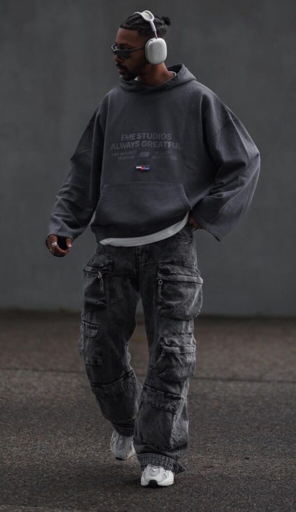 Man in streetwear outfit with gray hoodie, cargo pants, and headphones walking confidently on pavement.