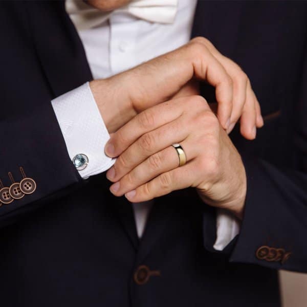 Man in formal suit adjusting cufflinks, wearing a wedding ring.