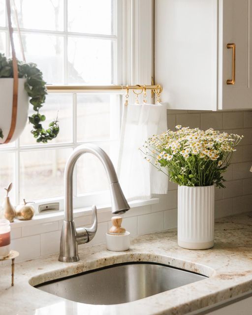 Sunlit kitchen sink with stainless faucet, potted flowers on counter, and bright window view. Inviting and fresh space.