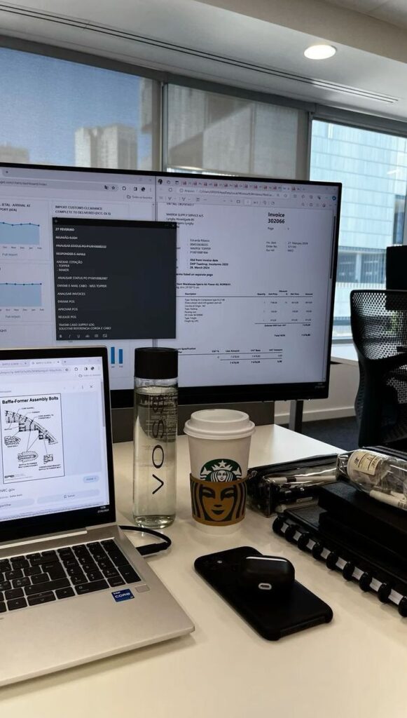 Office workspace with dual monitors, laptop, coffee, and water bottle on desk, set in a modern office environment.