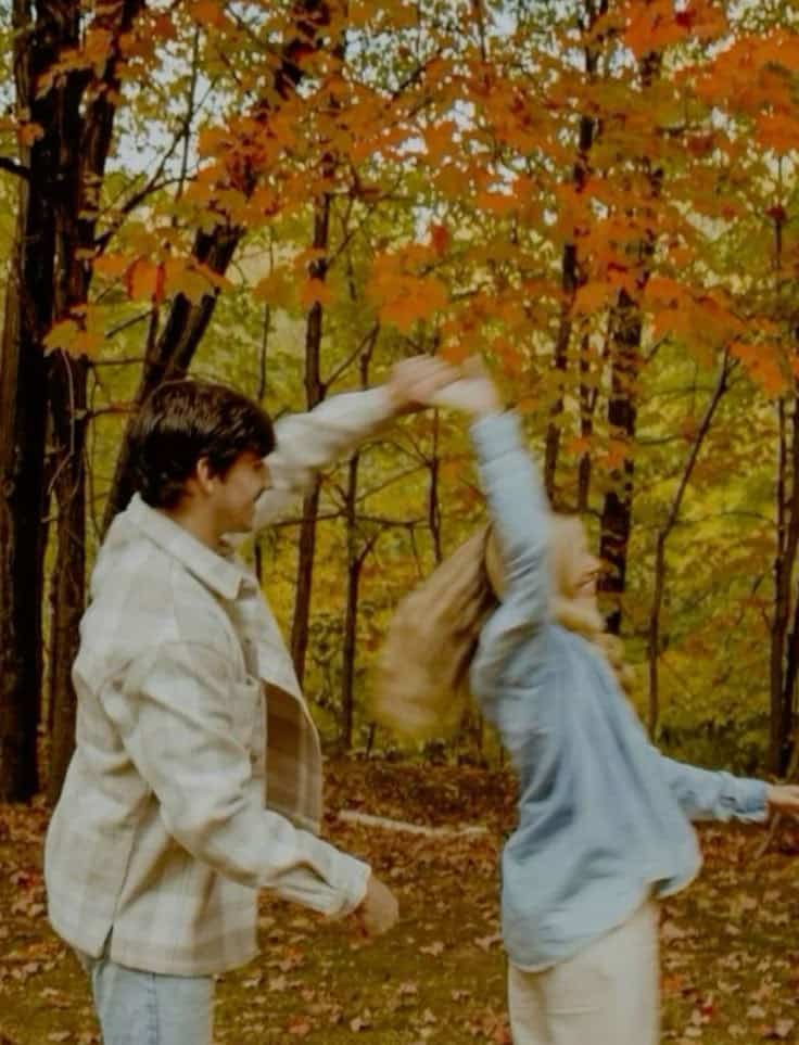 Couple dancing joyfully under vibrant autumn leaves in a forest setting, capturing the essence of fall romance.