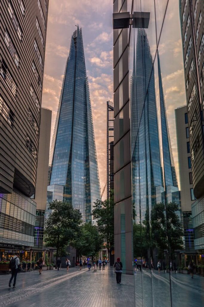 Skyline of modern glass skyscrapers with pedestrian walkway, under a colorful sunset sky.