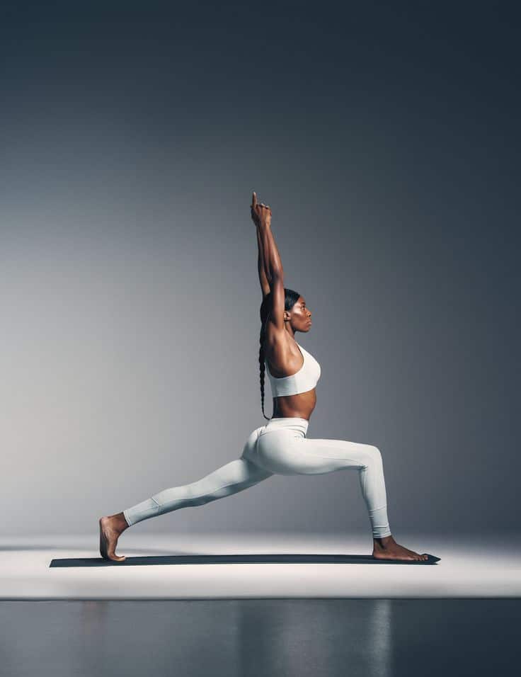 Person practicing yoga warrior pose on mat, wearing white workout clothes against a neutral gradient background.