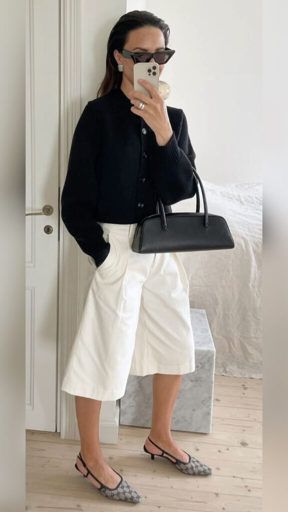 Chic outfit inspiration: black cardigan, white culottes, black handbag, and stylish heels. Mirror selfie fashion look.