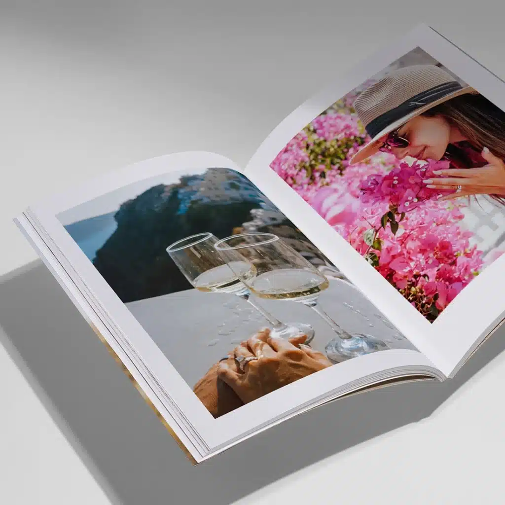 Open photo book with images of pink flowers and wine glasses on a sunny terrace.