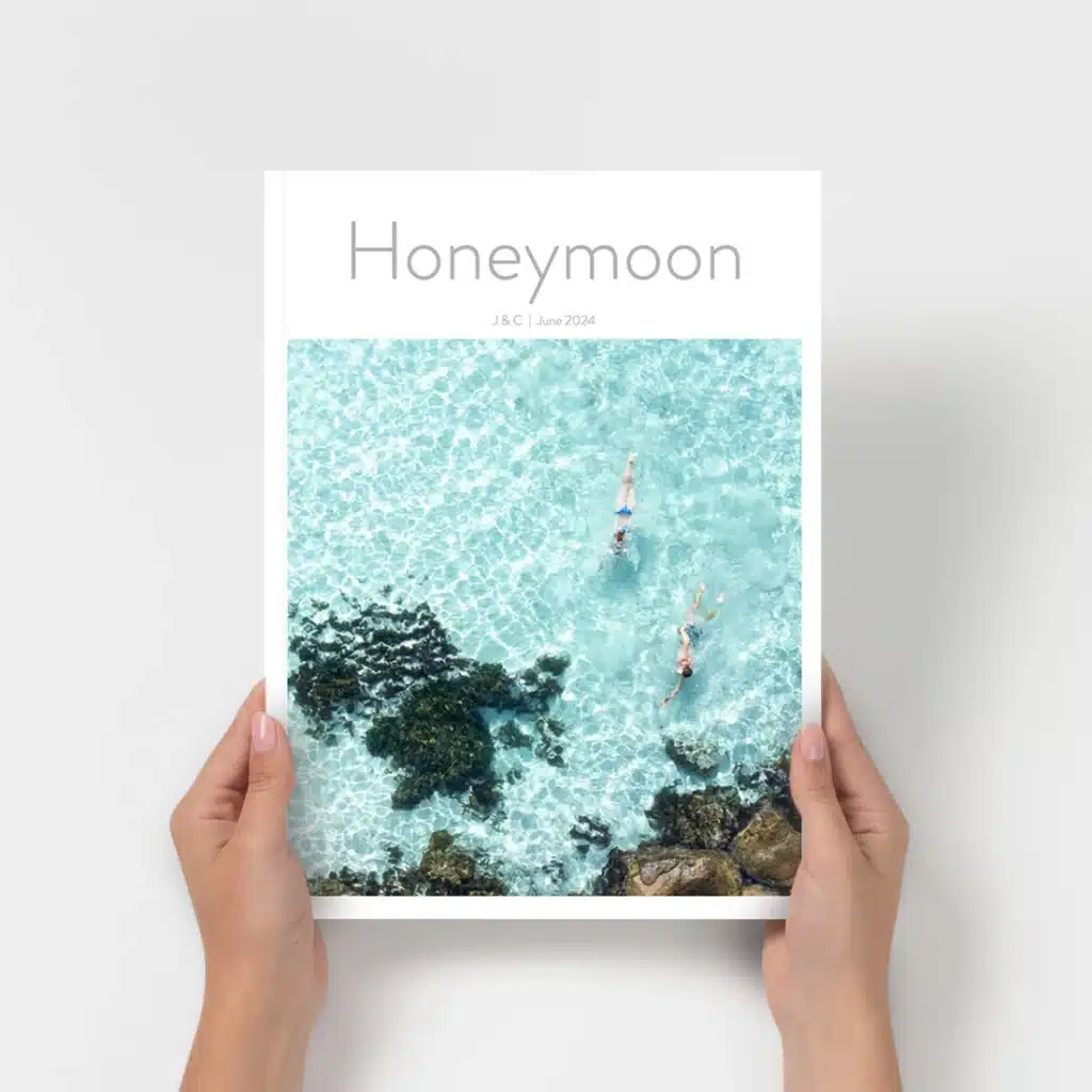 Honeymoon photo book cover showing two people swimming in clear turquoise waters with rocky formations.