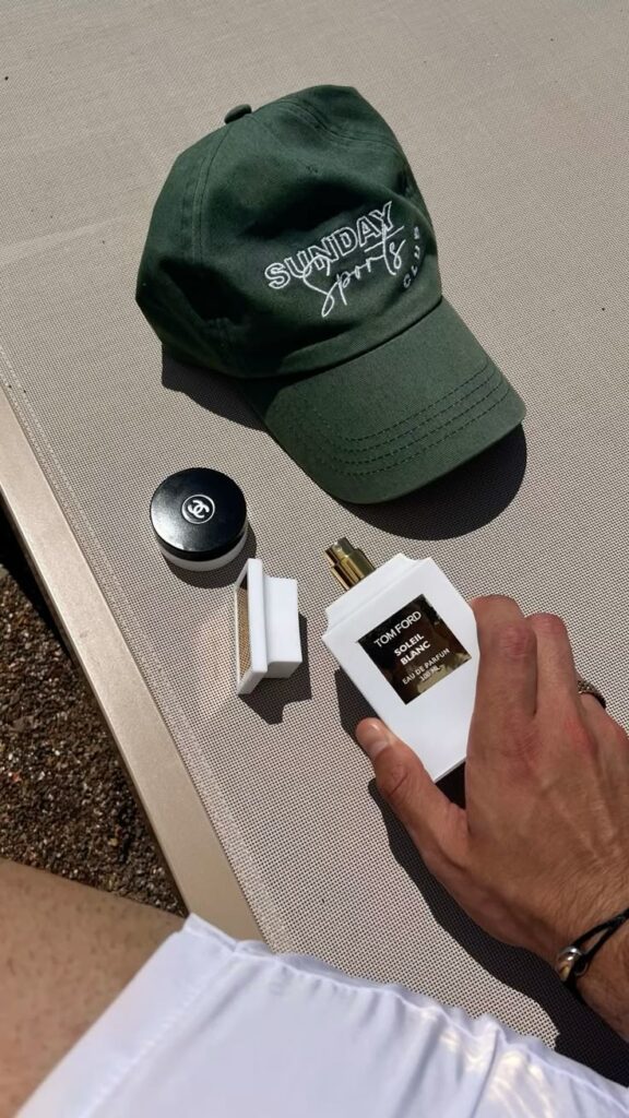 Green cap, Tom Ford perfume, Chanel product, and white clothing on a sunlit surface. Perfect summer essentials.