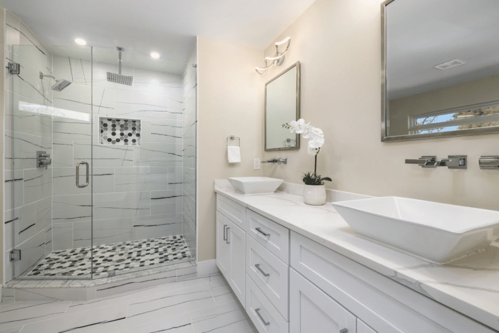Modern bathroom with glass shower, white vanity, vessel sinks, and orchid. Bright and elegant design.