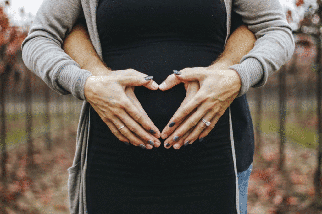 image A pregnant couple makes a heart with hands over the belly in an autumn vineyard setting. | Sky Rye Design A pregnant couple makes a heart with hands over the belly in an autumn vineyard setting.