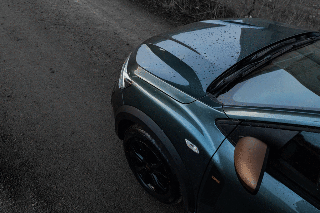 Sleek green car with raindrops on the hood parked on a gravel road, showcasing modern design and elegance.
