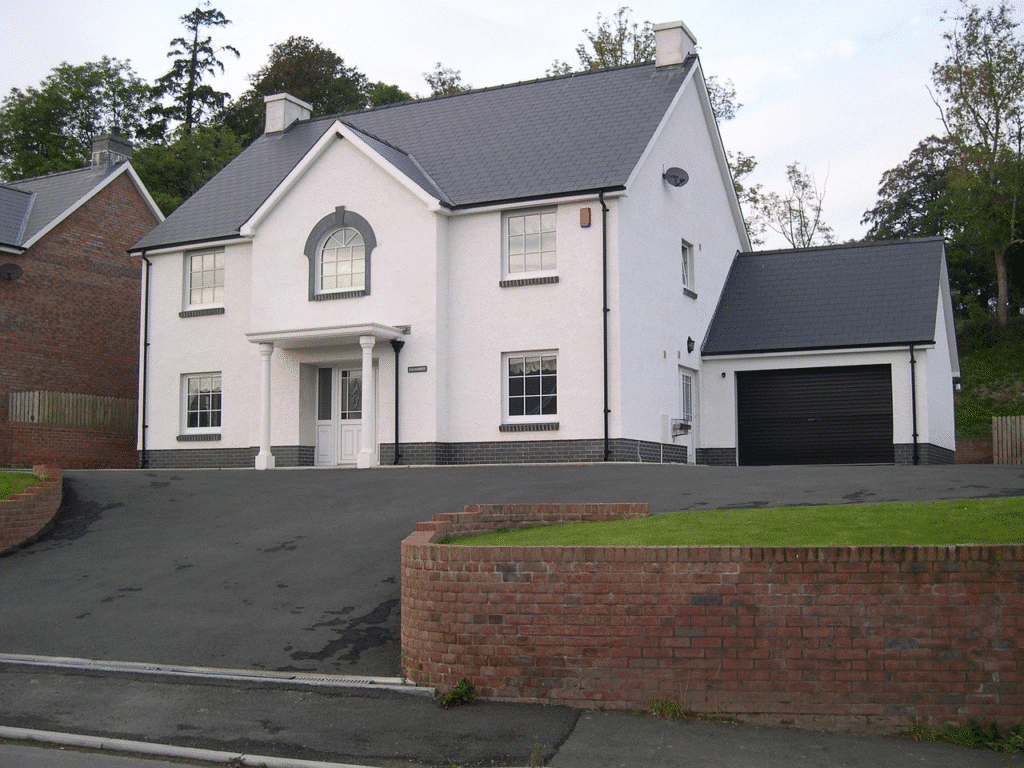 Elegant modern white house with driveway, garage, and well-maintained lawn, surrounded by trees and brick wall.