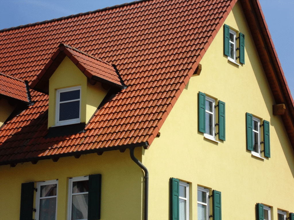 Yellow house with red tiled roof and green shutters in sunlight