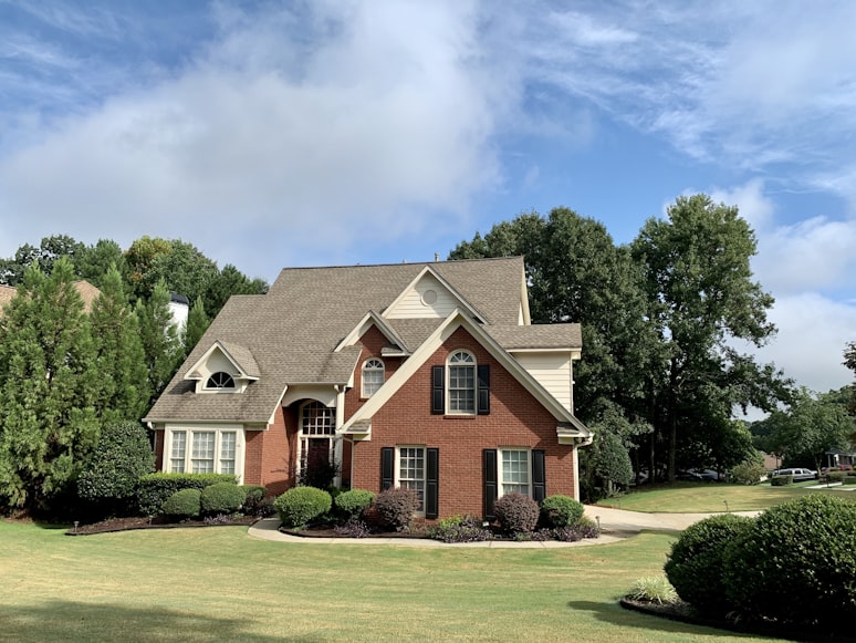 Brick suburban house with manicured lawn and trees under a blue sky.