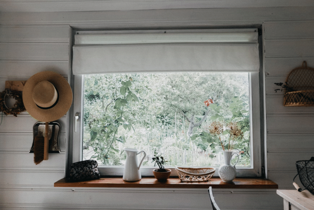 Cozy cottage window view with garden plants, a straw hat, and rustic decor on the windowsill.