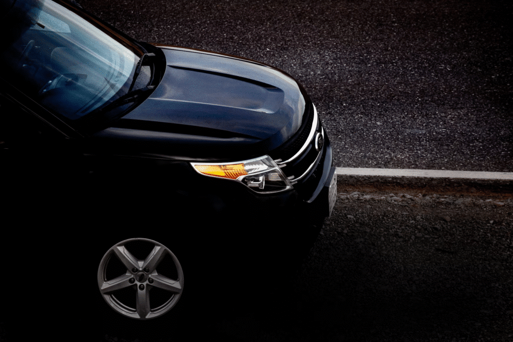 Close-up of a black car parked on a street, with its headlights and front wheel visible.