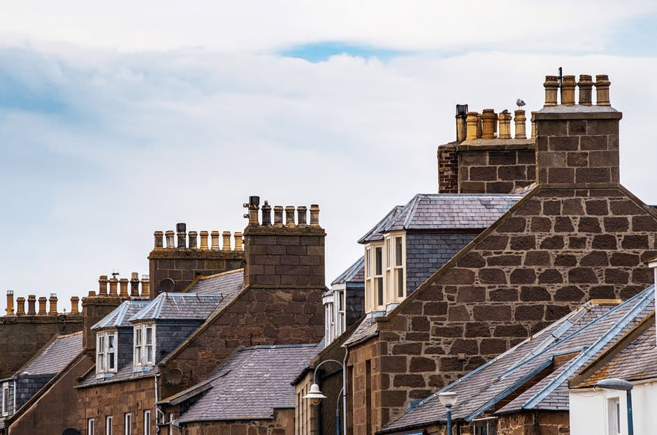 Rooftops with chimneys on old stone buildings under a partly cloudy sky.