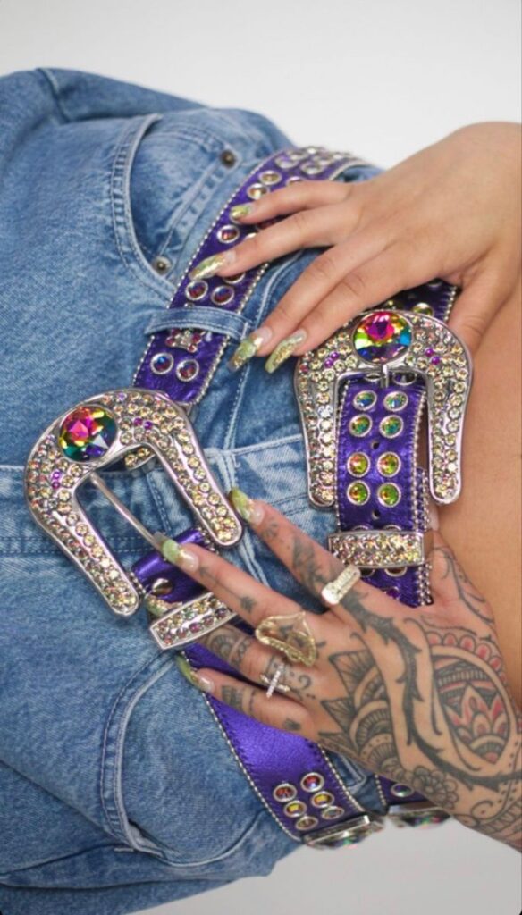 Close-up of a tattooed hand showcasing a jeweled purple belt and denim detail for a trendy fashion statement.