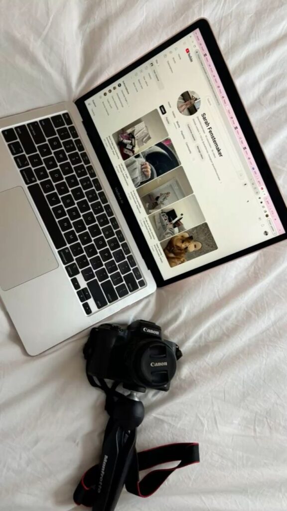 Laptop on bed displaying social media profile, with a camera and tripod beside it.