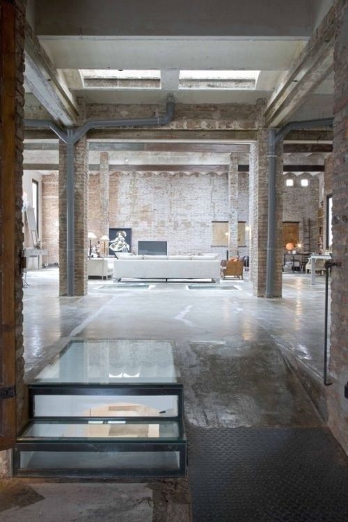 Industrial loft interior with exposed brick walls, large windows, and a modern minimalist design.
