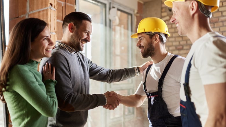Happy manual workers came to an agreement with a couple at construction site Two men shaking hands at a construction site, with colleagues smiling in the background. | Sky Rye Design Two men shaking hands at a construction site, with colleagues smiling in the background.