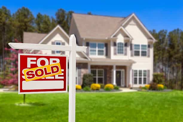Sign with Sold in front of a suburban house, blue sky, green lawn, real estate success.